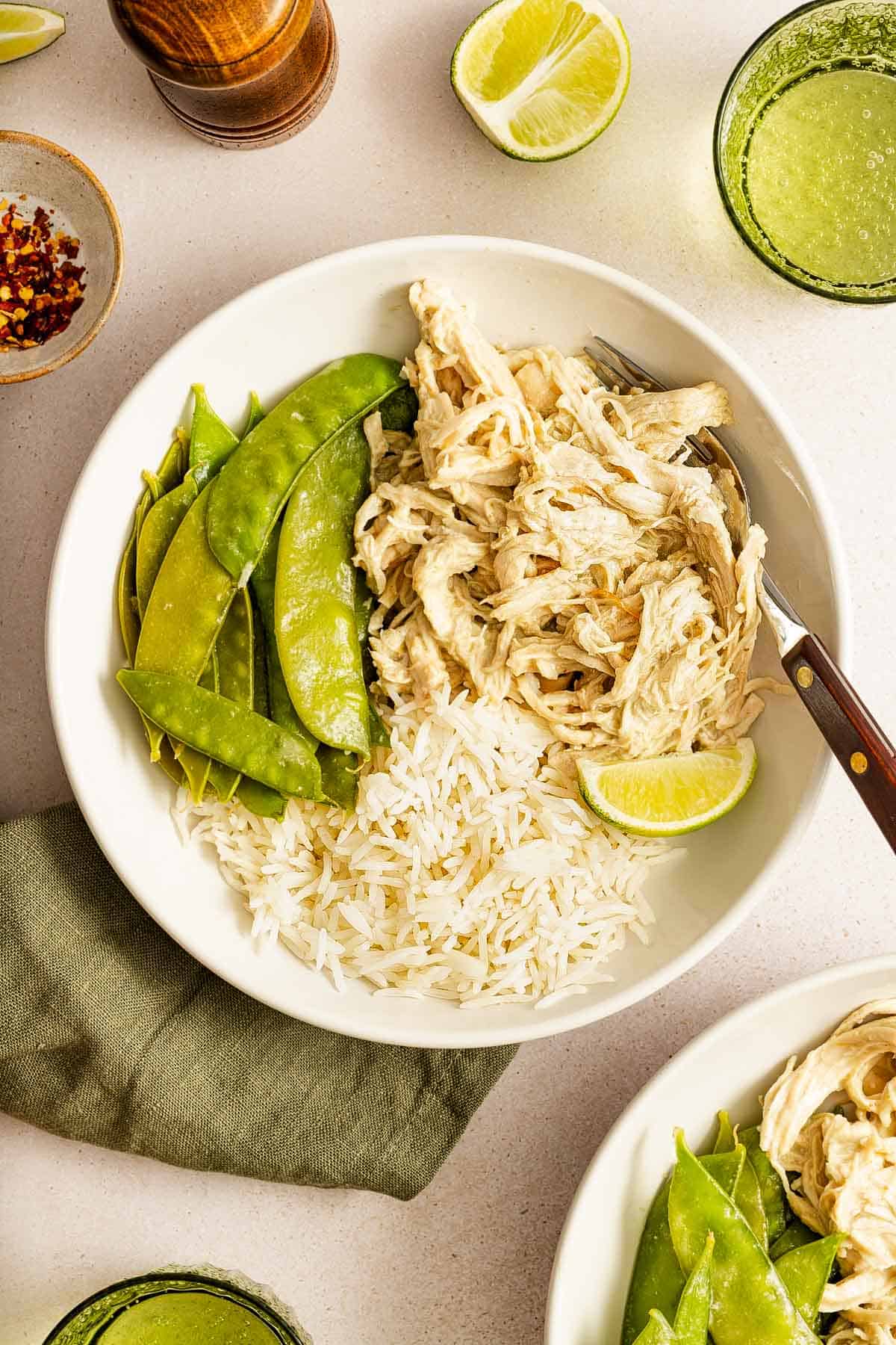 Overhead view of a bowl of rice and snow peas with shredded instant pot thai green curry chicken and a lime.