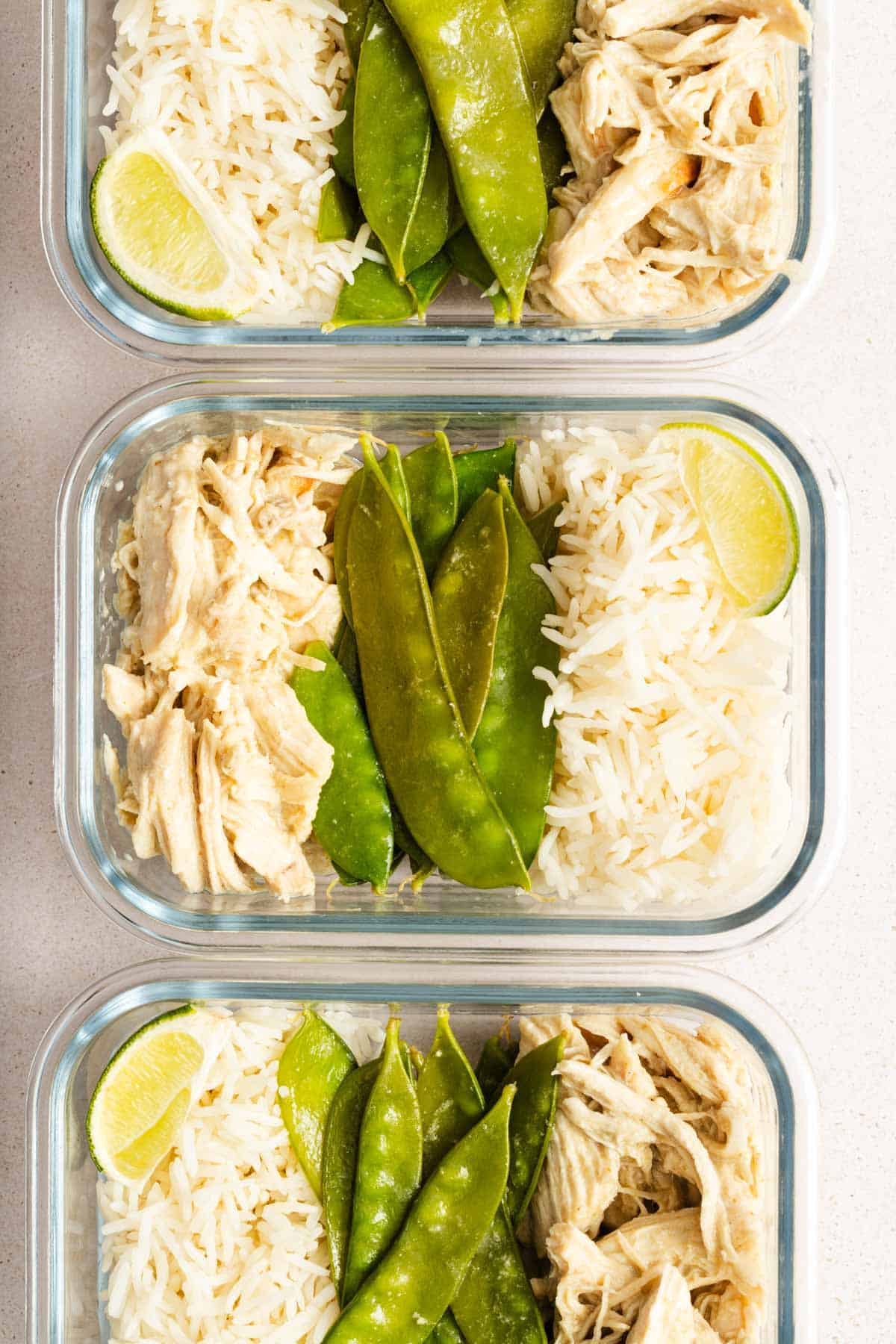 Meal prep containers with shredded instant pot thai green curry chicken, snow peas, rice, and lime wedges.