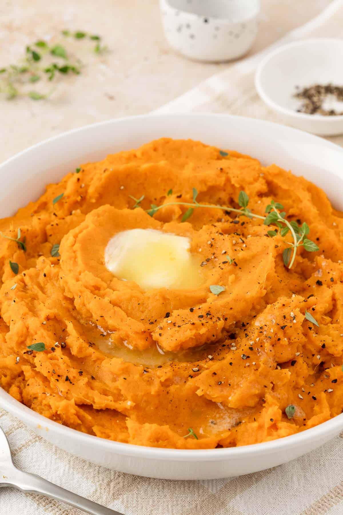 A bowl of mashed sweet potatoes with melted butter and fresh thyme as garnish.
