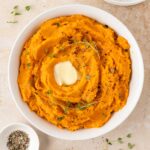 Overhead view of a plate of mashed sweet potatoes with melted butter and fresh thyme as garnish.