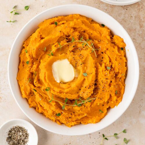 Overhead view of a plate of mashed sweet potatoes with melted butter and fresh thyme as garnish.