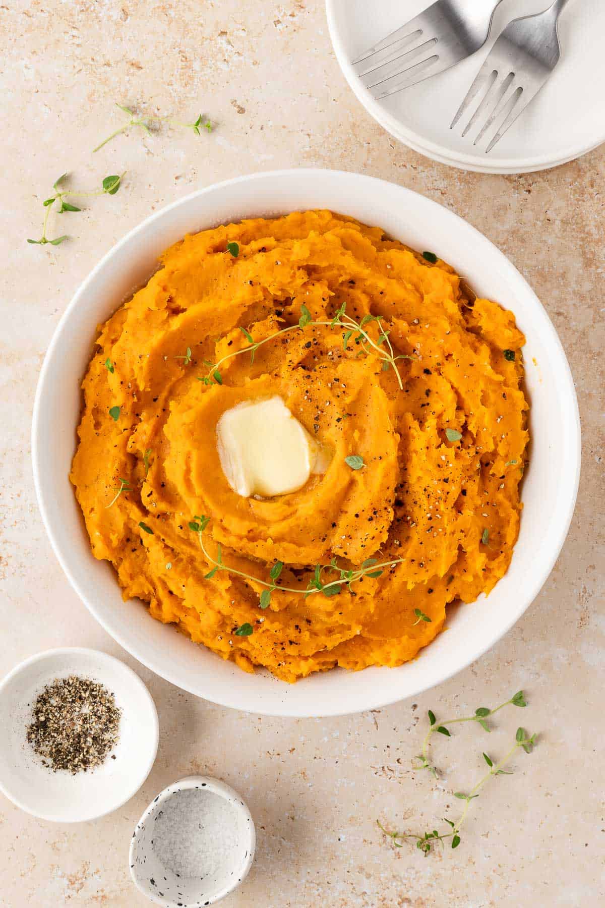 Overhead view of a plate of mashed sweet potatoes with melted butter and fresh thyme as garnish.